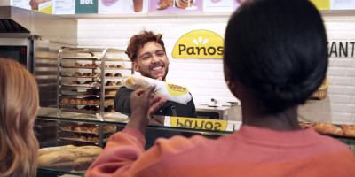 Panos werknemer levert Panos broodje aan een klant over de toog