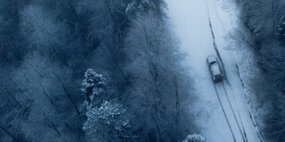 witte auto dat door het bos in de sneeuw rijdt